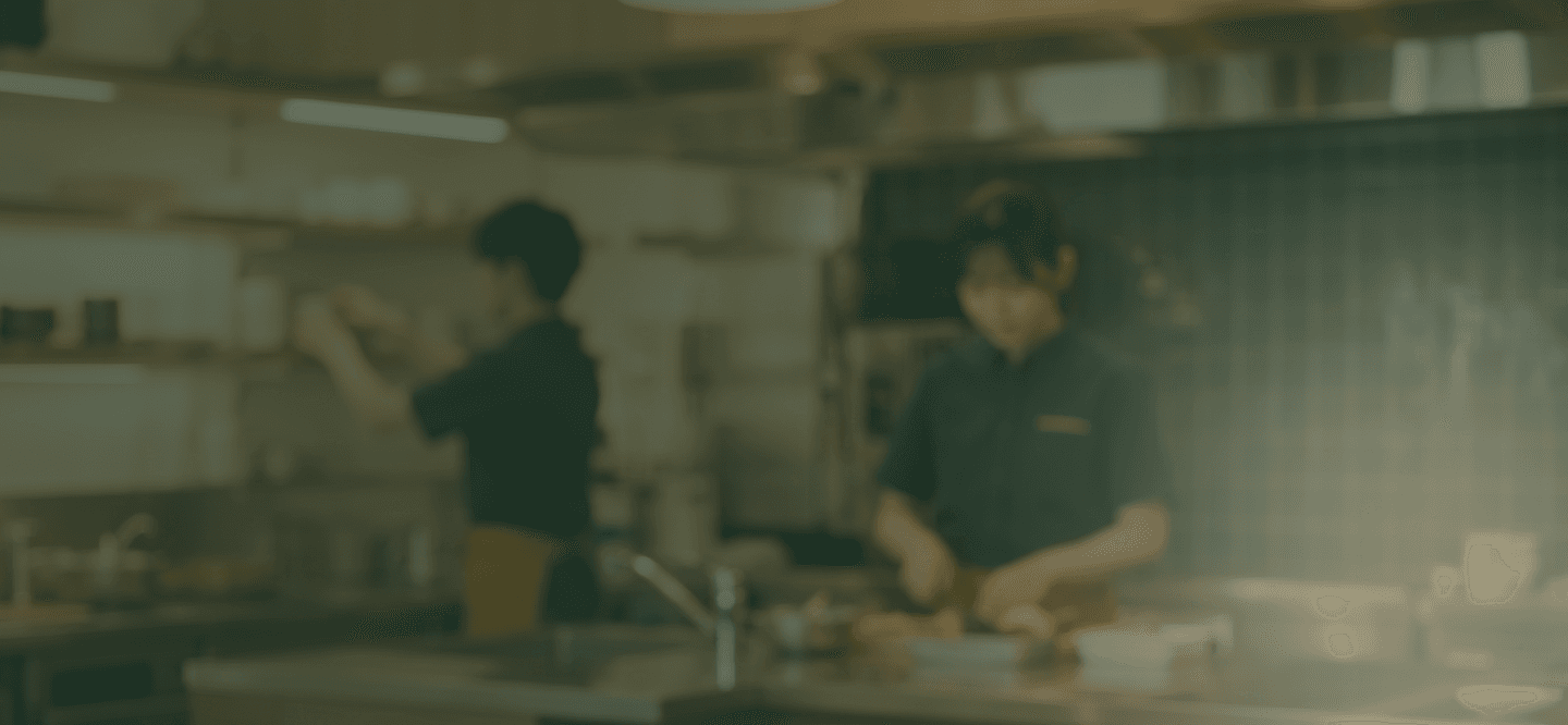 厨房で店舗スタッフが自分のスマホで人事CREWの入社手続き画面を操作している様子