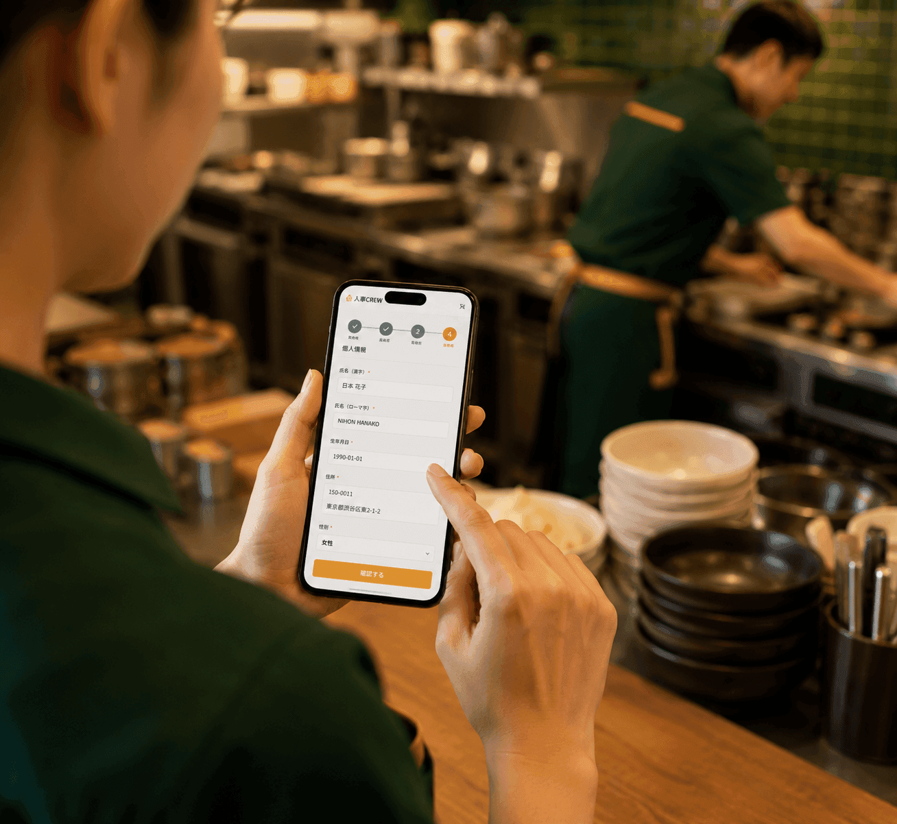 厨房で店舗スタッフが自分のスマホで人事CREWの入社手続き画面を操作している様子